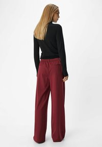 Zwarte aansluitende trui en burgundy wijde broek met elastische tailleband en achterzakken, met een soepele textuur en een relaxte silhouet.