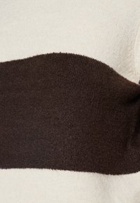 Pull en tricot avec un corps crème et une large bande horizontale marron foncé. Texture douce, présentant un col rond et des détails en côtes.