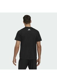 Camiseta deportiva negra de manga corta, con textura suave y el logo de Adidas en la parte posterior. Diseño sencillo, cuello redondo y ajuste relajado.