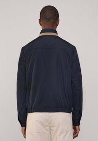 Cazadora bomber en azul marino de material ligero, con un cuello beige en contraste, dobladillo elástico y puños abotonados.