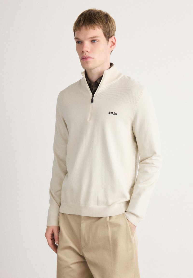 Pulover tricotat în bej deschis, cu guler tip quarter-zip și logo-ul negru "BOSS". Accente ribirikare pe umeri și manșete. Croi regulat, textură moale.