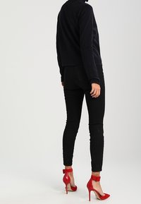 Černá zkrácená bunda, přiléhavé černé džíny a jasně červené vysoké podpatky s kotníkovými pásky. Hladká tkanina a elegantní design.