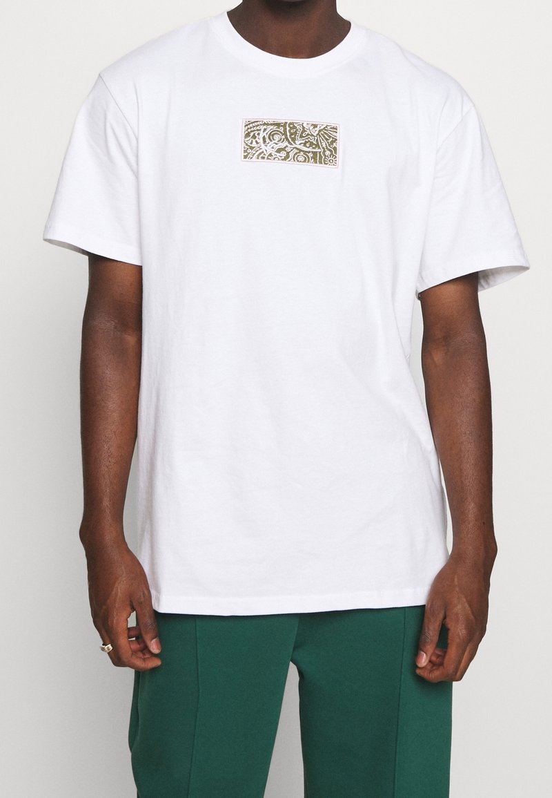 Bílý bavlněný tričko s krátkým rukávem, se vstavaným obdélníkovým khaki grafickým vzorem na hrudi s jemnými vzory. Hladký povrch.