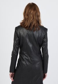Schwarze Lederjacke mit taillierter Silhouette, Schulterakzenten und langen Ärmeln. Glatte Textur und mittellange Ausführung, keine sichtbaren Verschlüsse.