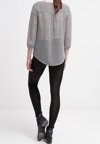 Blus med svart och vitt mönster, trekvartsärmar, genomskinlig textur och rundad fåll, kombinerad med svarta leggings och ankelstövlar.