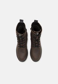 Botas de cuero marrón hasta el tobillo con punta redondeada, cordones negros y cremallera interior. Presentan un suave forro interior y una lengüeta para tirar.