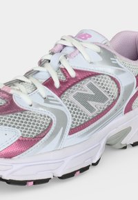 Chaussure de running New Balance blanche et rose avec panneaux en mesh, lacets blancs et semelle en caoutchouc texturée visible sur fond clair.