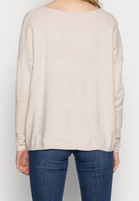 Pull en tricot beige clair avec un large col arrondi et un motif texturé sur les manches et les épaules ; ourlet côtelé, coupe décontractée.