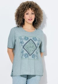 Camiseta de manga corta azul claro con un acabado texturizado, que presenta un estampado central en forma de diamante con motivo paisley en tonos verdes y azul marino.