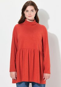 Dlouhý rukáv rolák v barvě spáleného pomeranče, s plisovanou spodní částí a kapsou na prsou. Měkká, lehká tkanina s volným střihem.
