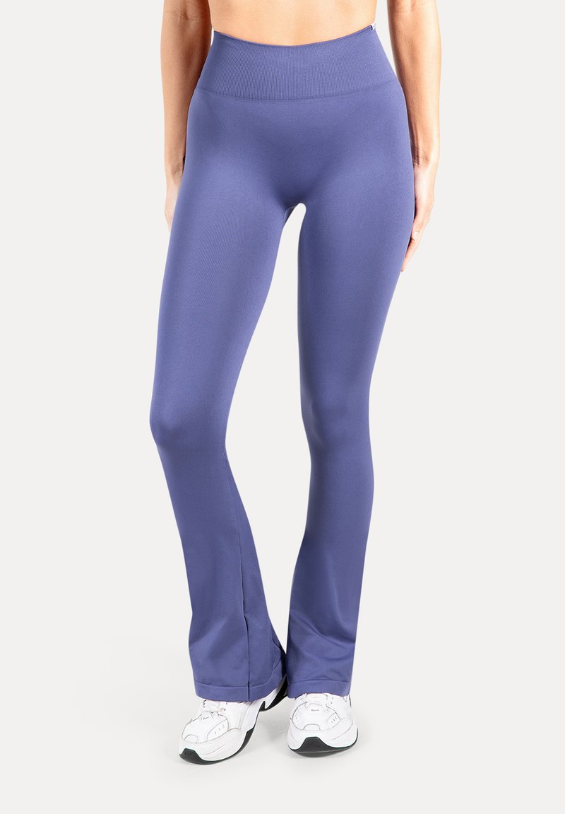 Leggings atletici aderenti viola con fascia alta in vita, realizzati in tessuto liscio; svasati alle caviglie, abbinati a scarpe da ginnastica bianche.