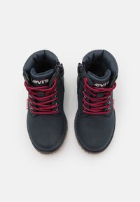 Černé kotníkové boty s červenými šnůrkami, polstrovaným límcem a strukturovanou gumovou podrážkou. Na jazyku a bočním štítku se nachází logo Levi's.