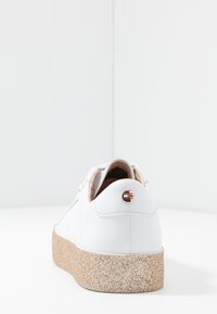 White leather sneaker with a textured, light brown sole and a rose gold accent on the back. Smooth finish and low-profile design.