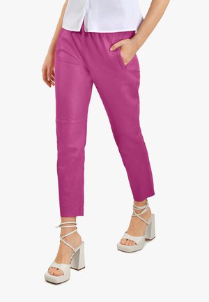 Pantalons roses à coupe fuselée avec poches avant, texture lisse et taille élastique, associés à des sandales à talons carrés blanches avec lanières.
