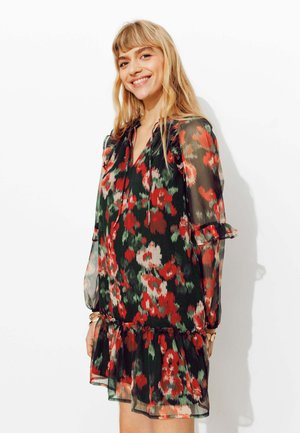 Robe à motif floral en tissu noir transparent avec des accents rouges et verts. Caractérisée par des manches à volants et un ourlet évasé. Encolure réglable.