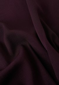 Približni posnetek globoko vijoličnega tkanega materiala z rebrasto teksturo, vidne teksture in gub, ki ustvarjajo mehke sence in poudarke.