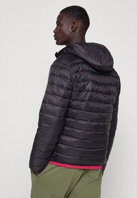 Giacca a vento nera con cappuccio, texture trapuntata, maniche di lunghezza media e chiusura con zip. Presenta una finitura leggermente lucida.
