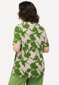 Camicia a maniche corte con un motivo floreale verde su sfondo beige, realizzata in tessuto morbido con un fit comodo.