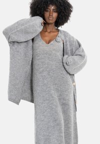 Szara dzianinowa sukienka swetrowa z dekoltem w serek, ozdobiona kwiatowymi akcentami, oraz luźny kardigan z dużymi rękawami i drewnianymi guzikami.