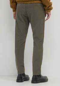 Olivgrüne Cordhosen mit geradem Schnitt, vertikalen Rippungen, zwei Gesäßtaschen und kombiniert mit schwarzen Lederstiefeletten.