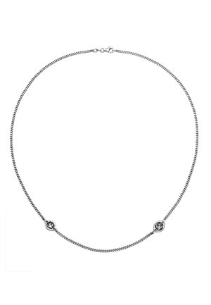 Zilveren ketting met een geweven textuur, met twee ronde metalen accenten in het midden. Sluiting aan de achterkant.