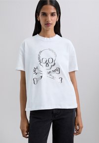 White cotton t-shirt featuring a skull and crossbones graphic with metallic accents, round neckline, and short sleeves.