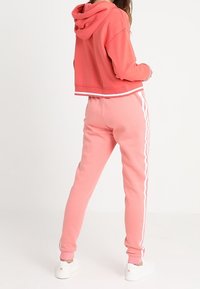 Huvtröja med kort längd och matchande joggers i mjuk rosa tyg. Joggers har vita sidosträck. Båda har en avslappnad passform.
