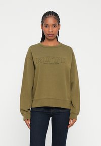 Felpa verde oliva con scollatura a girocollo e maniche lunghe. Presenta ricamata la scritta "MO’PD" e "Marc O'Polo DENIM" con cuciture scure.