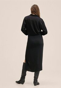 Vestido de satén negro con una silueta larga y ajustada. Presenta mangas largas, un cuello y aberturas laterales. Complementado con botas negras hasta la rodilla.