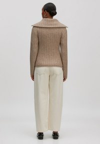 Beige gestreifter Pullover mit weitem Kragen, kombiniert mit off-weißen weiten Hosen und schwarzen Schuhen; Ansicht von hinten.