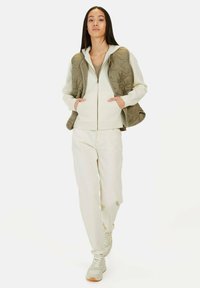 Beige gewatteerde vest over een witte hoodie, gecombineerd met crèmekleurige broeken en lichte sneakers, met een relaxte pasvorm en een minimalistisch ontwerp.