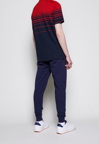 Camicia a maniche corte a righe rosse e blu abbinata a jogger blu e sneakers bianche. La camicia presenta righe orizzontali nella parte superiore.
