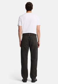 Jeans di denim neri con taglio dritto, dettagli di cucitura visibili e due tasche posteriori. Indossati con una t-shirt bianca semplice e scarpe nere.