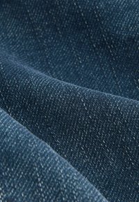 Sötétkék farmer anyag, szövetes textúrával, sima felszínnel és enyhe rugalmassággal, melyen világos foltok találhatók.