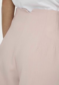 Pantalones de tiro alto en rosa claro con una cintura en forma de V y detalles de costura visibles, hechos de una tela suave y texturizada.