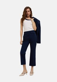 Granatowe, krótkie spodnie w połączeniu z białym topem bez rękawów z falbaniastym dekoltem, dopełnione granatowym żakietem zarzuconym na jedno ramię. Beżowe buty na obcasie.