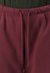 Burgundske trenirke s pojasom na vezanje, od mekanog pamučnog materijala i glatke teksture, sa ušivenim detaljima duž šavova.