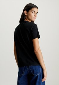 T-shirt nera in cotone con colletto tondo classico, maniche corte e vestibilità comoda, abbinata a jeans in denim blu. Vista posteriore mostrata.