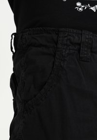 Black cargo pants featuring a smooth fabric, elastic waistband, side pockets, and stitched seams. The design is relaxed fit with adjustable details.
