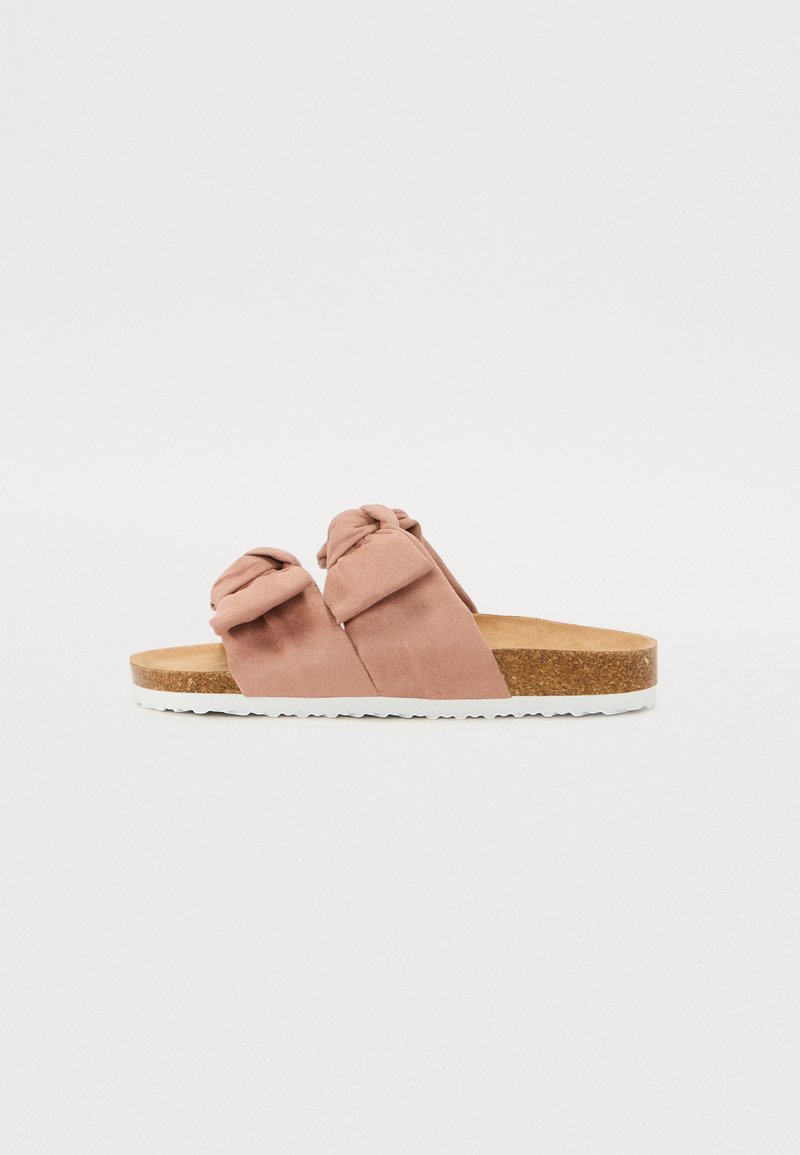 Le ciabatte slide in suede rosa presentano due cinturini annodati, un sottopiede in sughero e una suola in gomma bianca con dettagli testurizzati per una presa migliore.