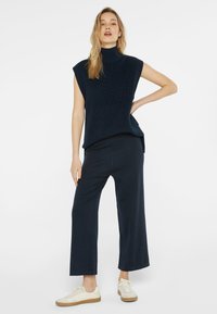 Navy-gestreifter ärmelloser Rollkragenpullover kombiniert mit einer lockeren, weiten Hose. Die Person trägt off-white Sneakers.