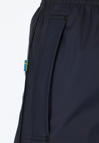 Marineblau wasserfeste Hose mit einem elastischen Bund, Seitentasche mit Druckknopf und einem kleinen blauen und gelben Emblem. Glatte Textur.