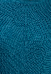 Skrzyżowany sweter w kolorze teal z teksturowanym wzorem i okrągłym dekoltem. Tkanina ma gładkie, jednolite sploty.