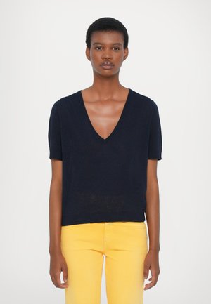 Marineblå kortermet genser med dyp V-hals og ribbestrikket kant. Lett, myk stoff med lett tekstur, kombinert med gule jeans.