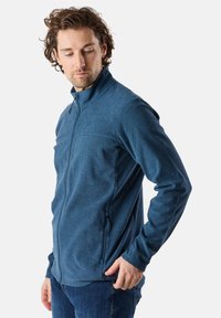 Herrblå fleecejacka med hög krage, zippered front, sidofickor och en texturerad tyg. Har en figursydd design och subtil logotypdetalj.