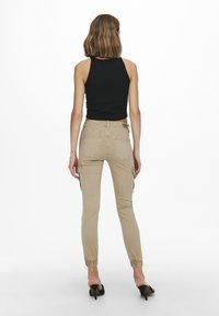 Beige cargo pants with a tapered fit, elastic cuffs, side pockets, and a mid-rise waist, paired with a black sleeveless top.