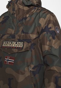 Jakke med camouflage-mønster, frontlynlås, Napapijri Geographic logo-patch, norsk flagg patch og rund logo-patch på ærmet.