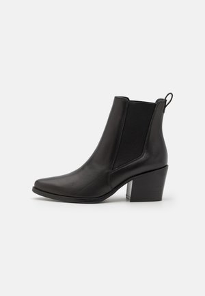 Botas de cuero negro hasta el tobillo con punta afilada, paneles laterales elásticos y tacón bloque de altura media. Cuenta con una lengüeta para ponérselas fácilmente.