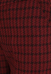 Rood en zwart houndstooth-patroon stof met een gestructureerd oppervlak, dat een klassiek geweven ontwerp en rijke kleurcontrasten toont.