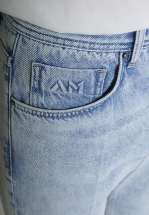 Primo piano di jeans in denim azzurro chiaro con una piccola tasca frontale che presenta lettere ricamate sul tessuto.